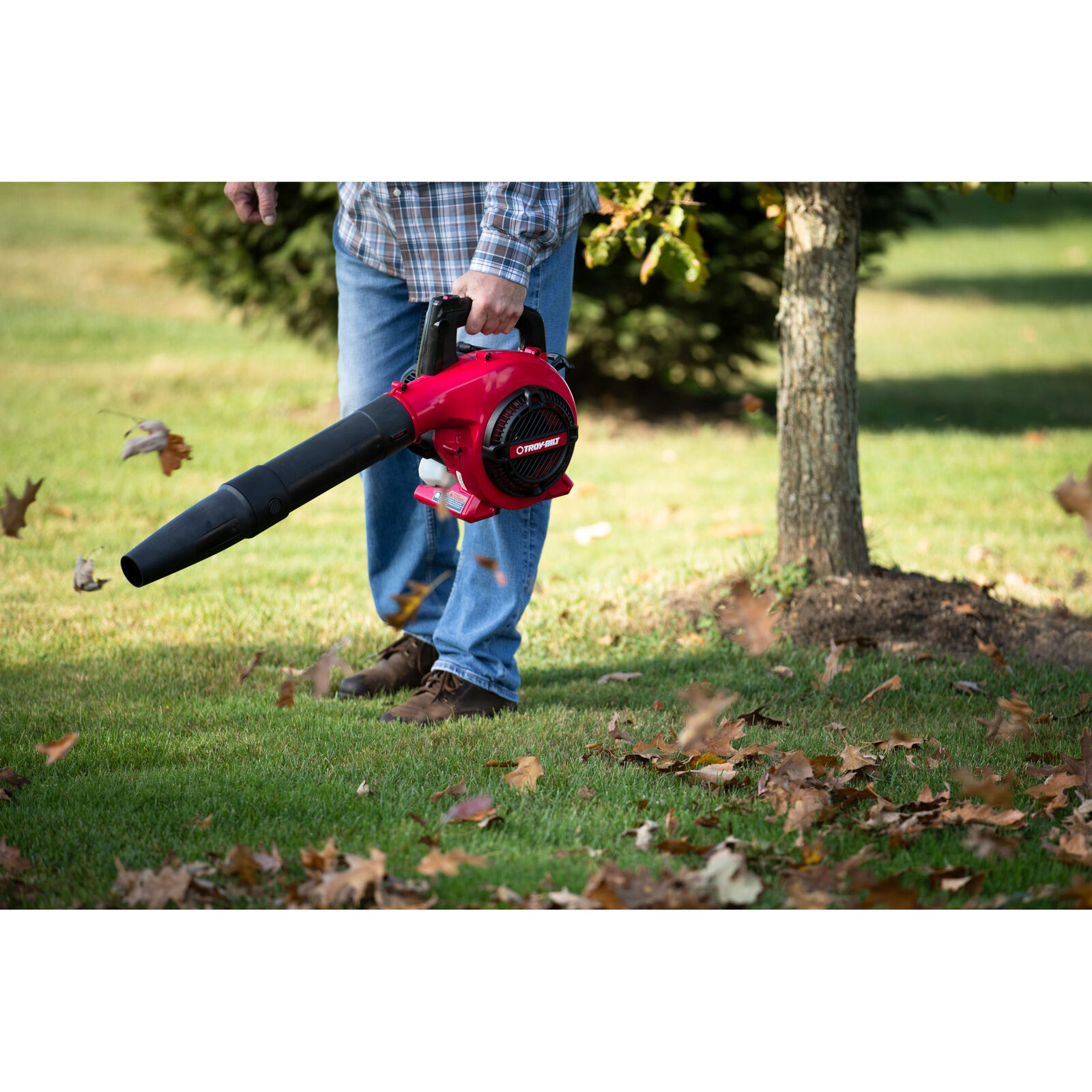 Troy-Bilt TB400 leaf blower pushing leaves away from a tree trunk on a green lawn