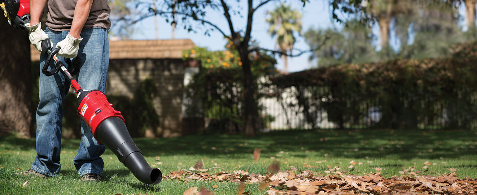 Person using TrimmerPlus blower attachment to blow leaves off lawn