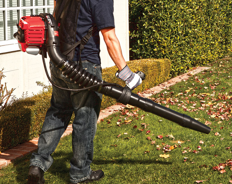 man using backpack leaf blower to blow leaves off lawn