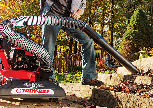 person using hose on chipper shredder vac to clean up leaves on stone steps