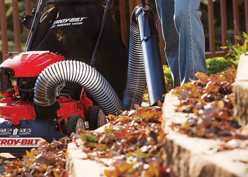 person using hose on chipper shredder vac to clean up leaves on stone steps