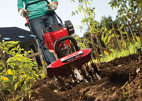 Woman using gas-powered cultivator to cultivate garden soil for planting