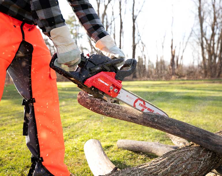 man cutting fallen limbs in wooded area with Troy-Bilt tree trimming tools