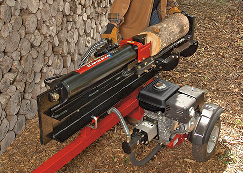 person using log splitter in front of wall of stacked wood logs